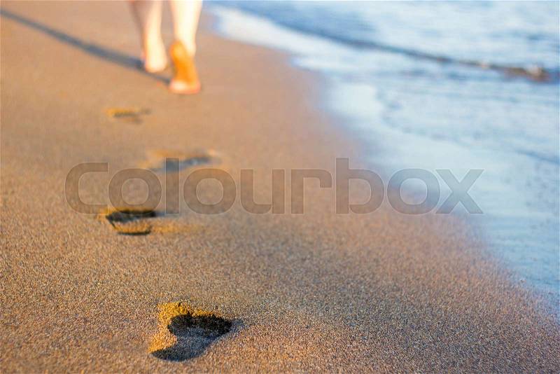 Summer end - close up of female legs and footprints on the sunset beach in warm country, stock photo