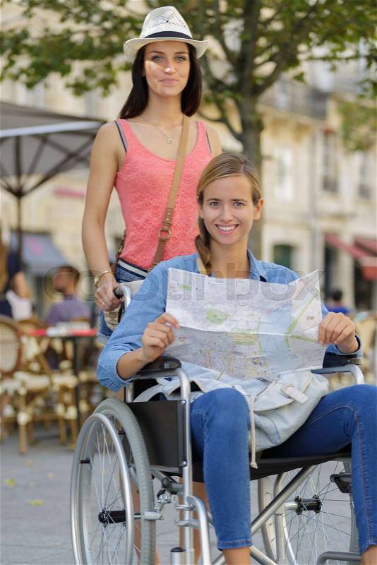 Two friends visiting foreign city one sitting in wheelchair, stock photo