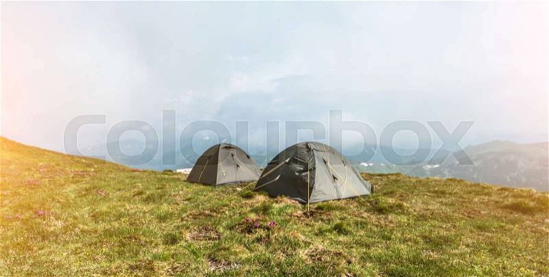 Tourist tents in camp among meadow in the mountain. Camping outdoor, tents in mountains, stock photo