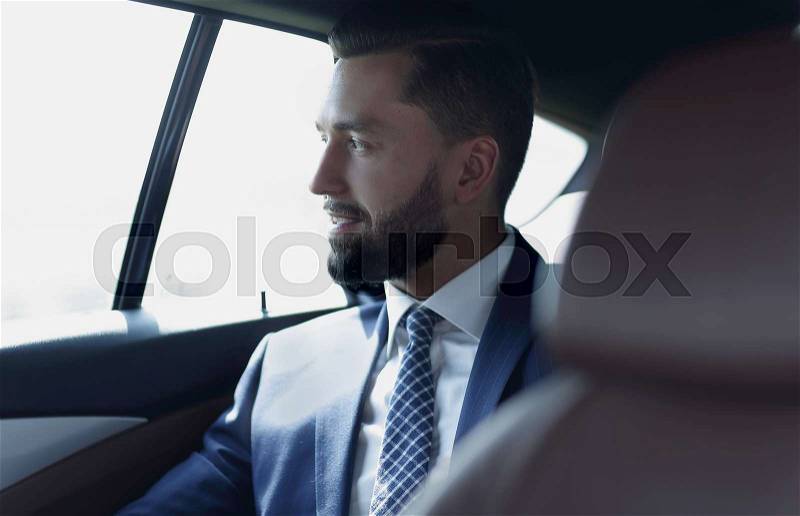Smiling successful man sitting in the back seat of a car, stock photo