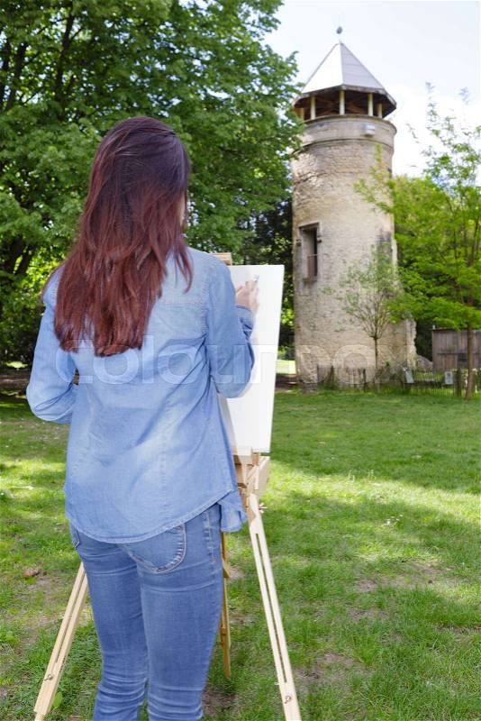 Young woman painting on canvas outside, stock photo