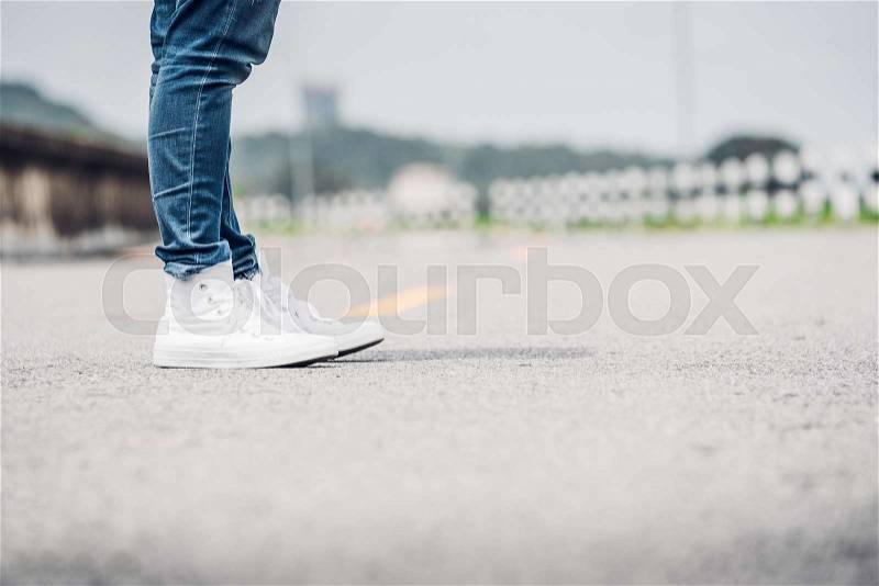 Close up woman wear jean and white sneaker standing on highway road in sunny day,Alone travel or solo traveler concept, stock photo