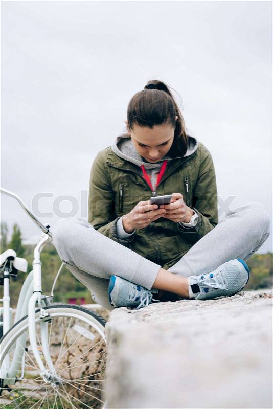 Young woman in a green jacket checks her mobile phone outdoors in autumn, stock photo