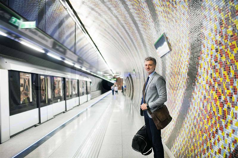 Handsome mature businessman in a city. Man waiting for the train at the subway station, stock photo
