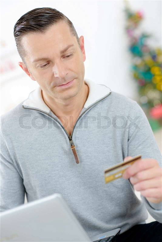 Man at laptop holding credit card, christmas tree in background, stock photo