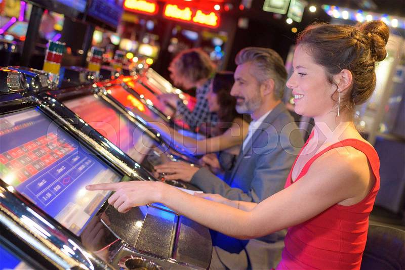 Happy woman sitting at slot machine in casino parlour, stock photo