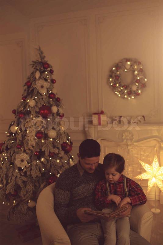 Father and son reading book near Christmas tree at home, stock photo