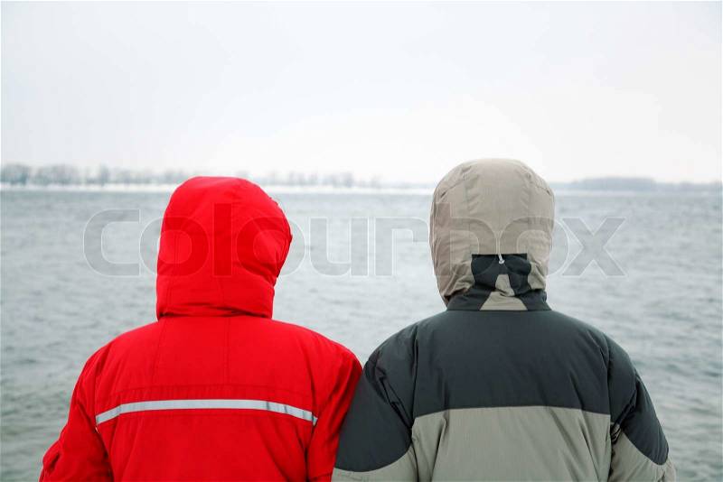 Two people in jacket with hood on the river background, stock photo