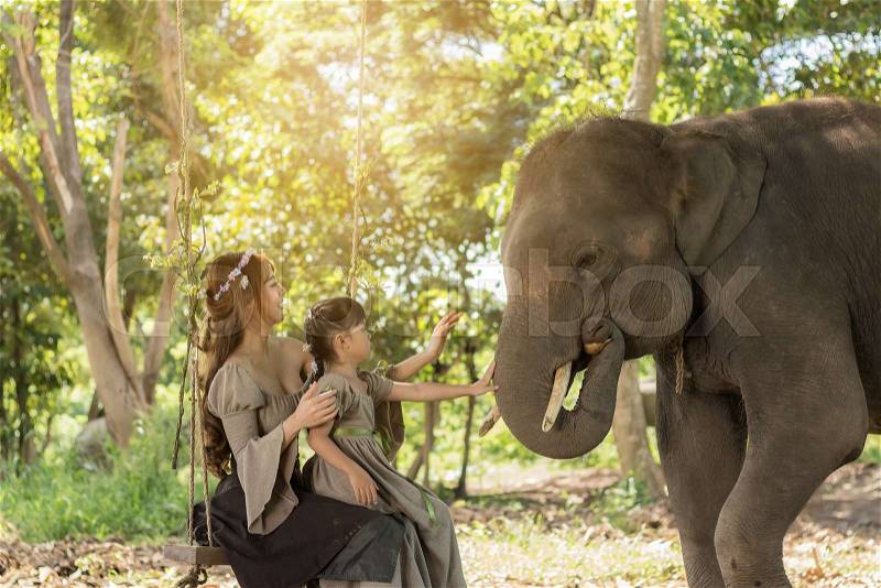 Portrait art of beautiful woman and girl playing with elephants in nature, stock photo