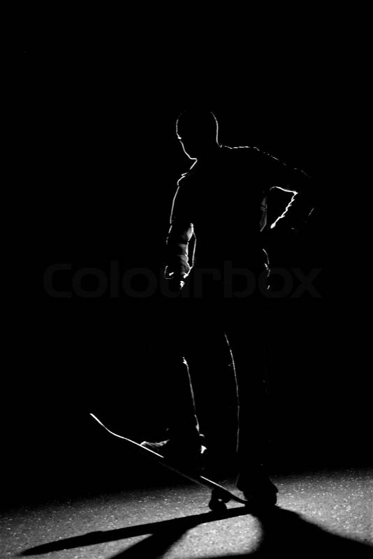 A rim lit skateboarder guy posing under dramatic back lighting with his skateboard flipped up in the front, stock photo