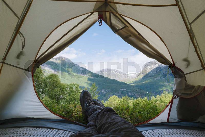 View from the tourist tent to the mountains. Guy in the boots lies on the rug, stock photo
