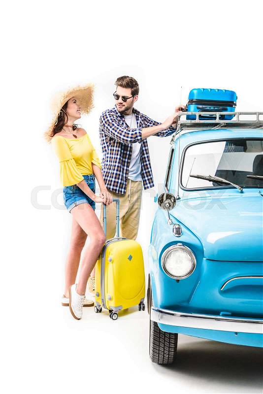 Cheerful young couple of travelers putting luggage on car roof isolated on white, stock photo