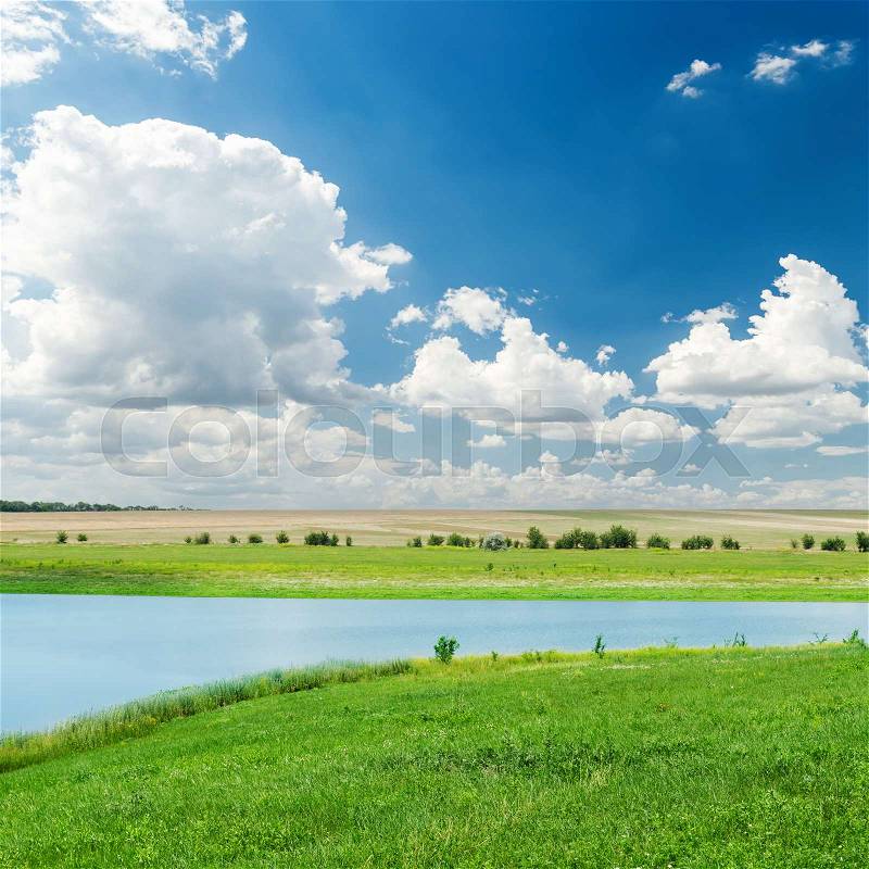 River in green grass and clouds over it in deep blue sky, stock photo