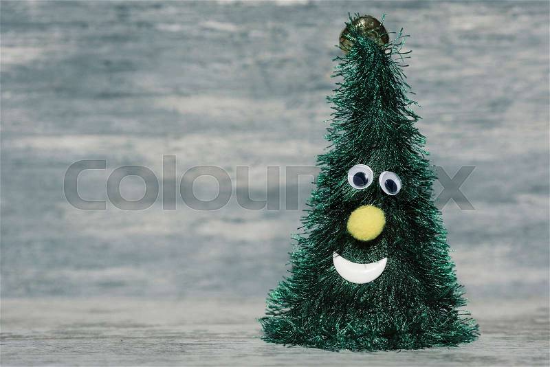 A christmas tree with a funny face against a gray rustic wooden background, with a blank space on the left, stock photo