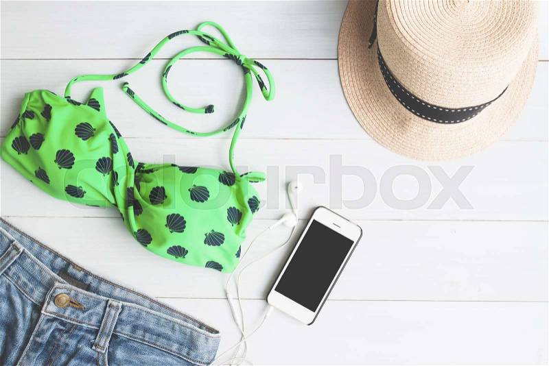Overhead view of bikini and short jeans, girl accessories with smartphone on white wooden background, Summer travel concept, stock photo