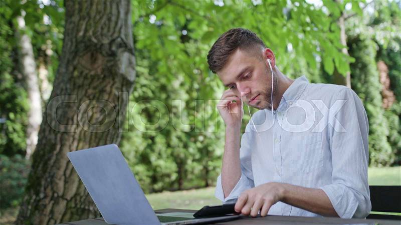 A young man listening to music on the phone in the park. Medium shot. Soft Focus, stock photo