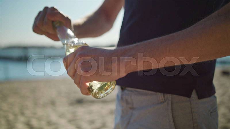A young man on the beach opening a bottle. Closeup shoot. Soft focus, stock photo