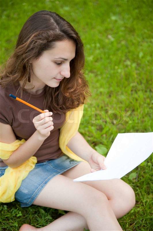 Young female is making notes in college lawn, stock photo