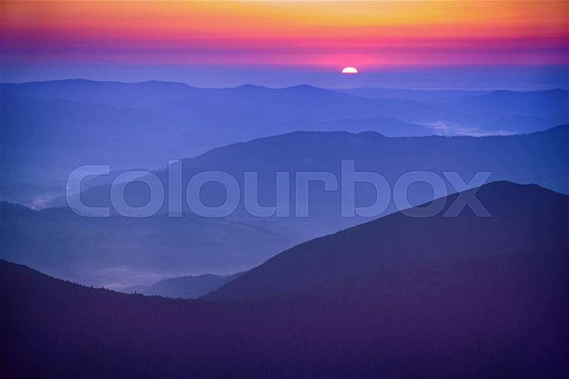 Amazing mountain landscape with colorful vivid sunrise on the bright sky over blue hills, natural outdoor travel background, stock photo