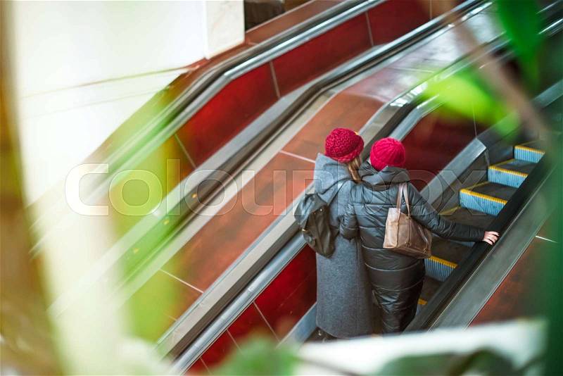 Back view two girls moving up on escalator in subway. Escalator in metro. Moving up staircase. electric escalator. View through the greenery. Selective soft focus, stock photo