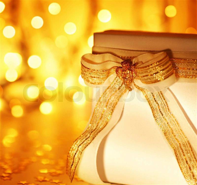 Gold holiday background with white present gift box, Christmas ornament and new year decoration over abstract defocused lights, stock photo