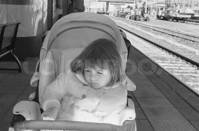 Baby girl in warm jacket sitting in modern stroller in the railway station. Traveling with young kids. Transportation for family with infant, infrared view, stock photo
