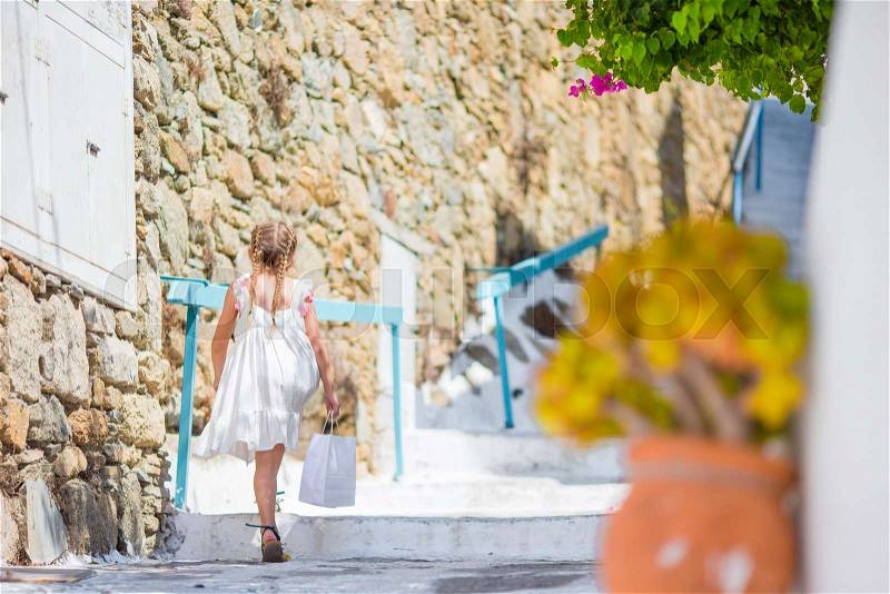 Adorable girl outdoors in greek village. Kid at street of typical greek traditional village with white stairs on greek island, stock photo