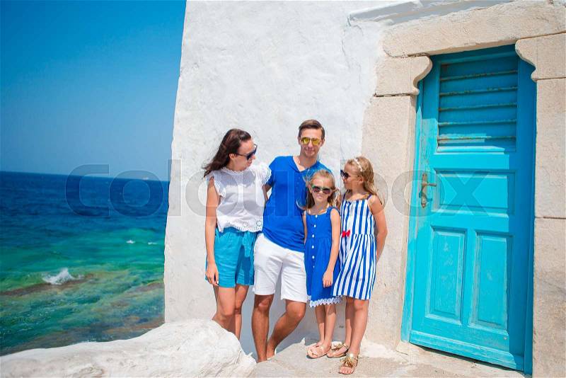 Family vacation in Europe. Parents and kids at street of typical greek traditional village with white walls and colorful doors on Mykonos Island, in Greece, stock photo