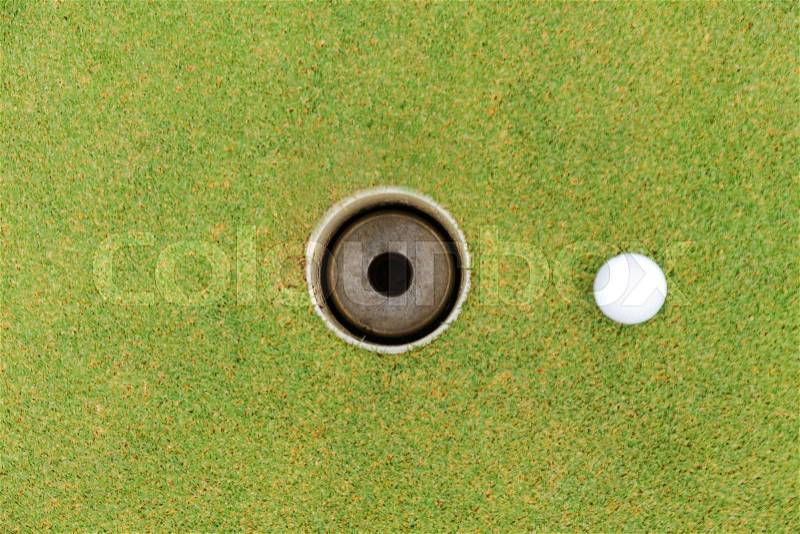 Golf hole and golf ball on green grass on golf course, stock photo