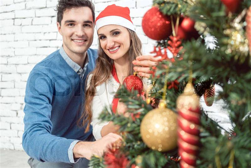 Couple at home decorating tree for Christmas with ornaments, stock photo