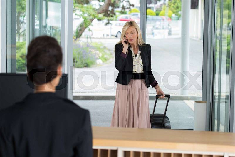Businesswoman arriving at the hotel welcomed by receptionist, stock photo
