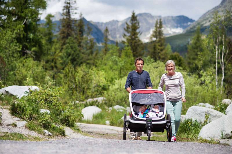 Senior couple and children in jogging stroller, summer day. High mountains in the background, stock photo