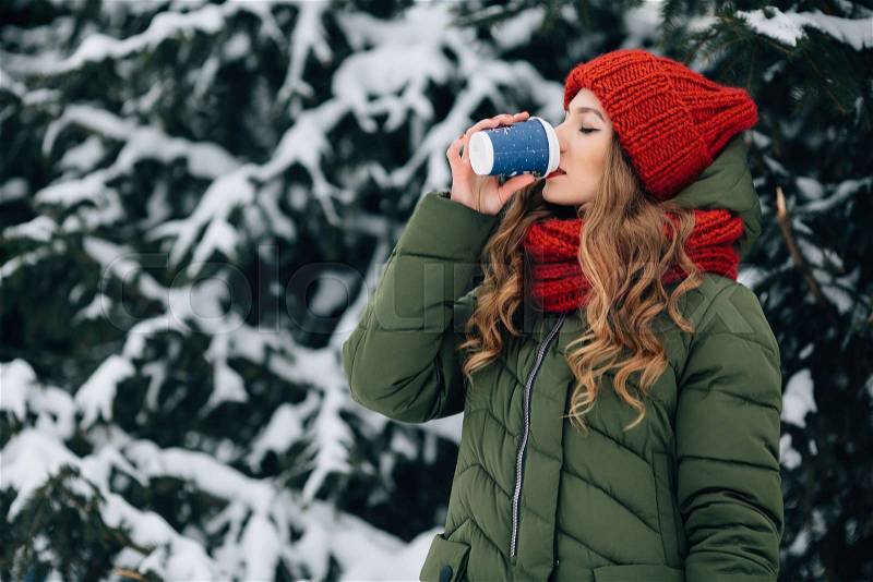 Winter coffee outdoors. Woman in warm winter clothes drinks coffee outdoors in winter snowy day. Woman with coffee, stock photo