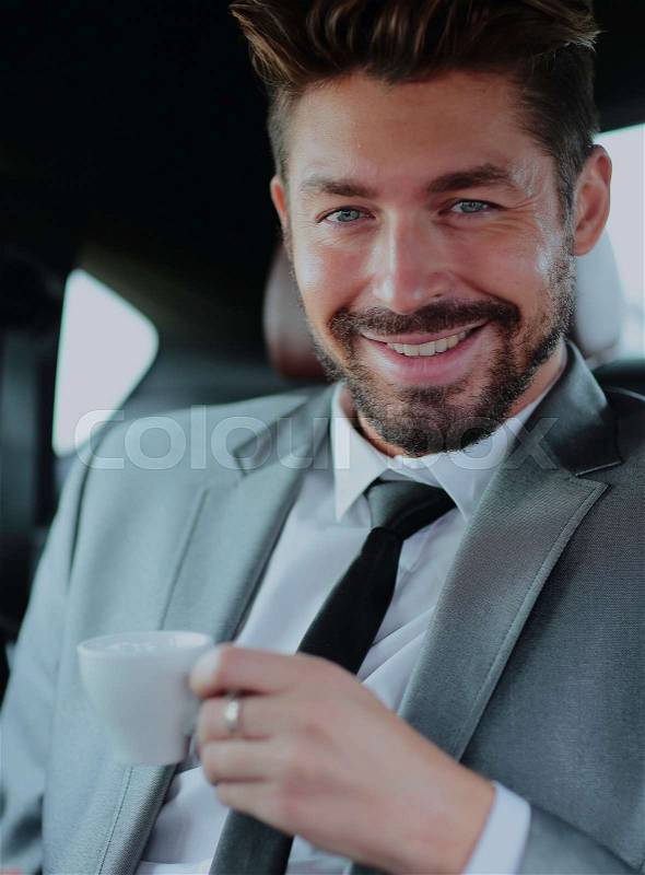 Smilinf successful businessman having a coffee in his car, stock photo