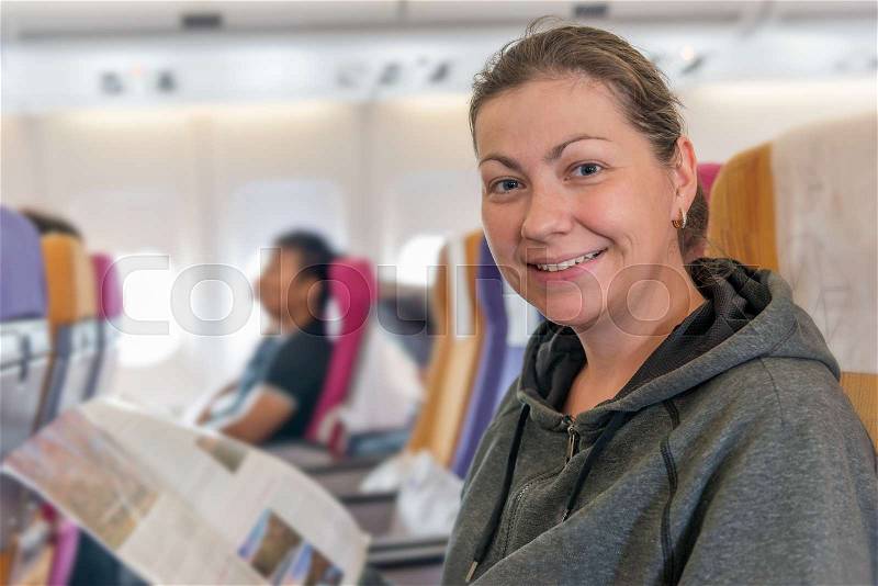 Happy airplane passenger with magazine in chair smiling during flight, stock photo