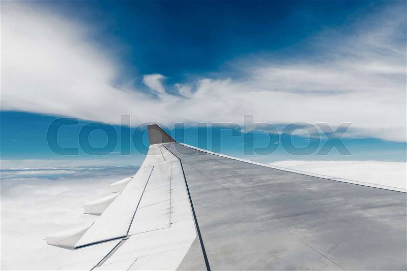Steel wing of the airplane close-up and light clouds at high altitude, stock photo