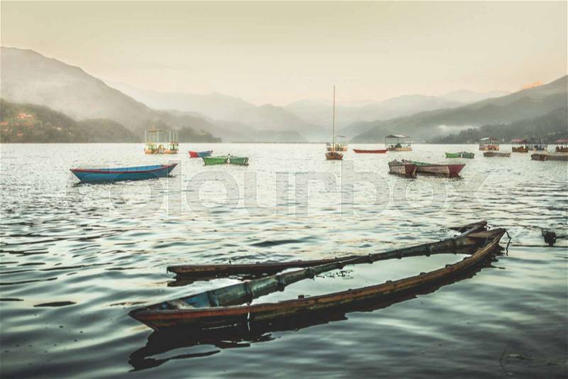 Colorful boats on Phewa lake at sunset. Sunk boat on the foreground, stock photo