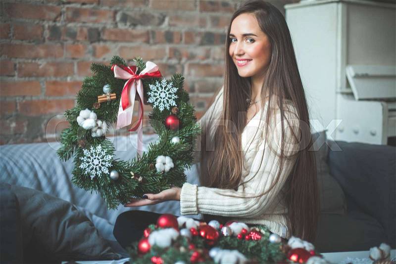 Young Cute Woman Florist with Christmas Tree Wreath with Red Glass balls, Ribbon and White Snowflake, stock photo
