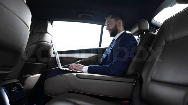 Side view confident businessman sitting on the backseat of a prestigious car, stock photo