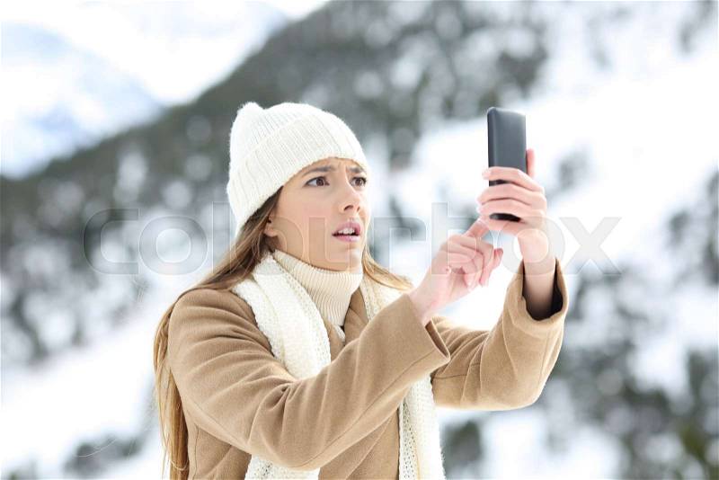 Desperate woman searching mobile phone coverage in winter holidays in a snowy mountain, stock photo