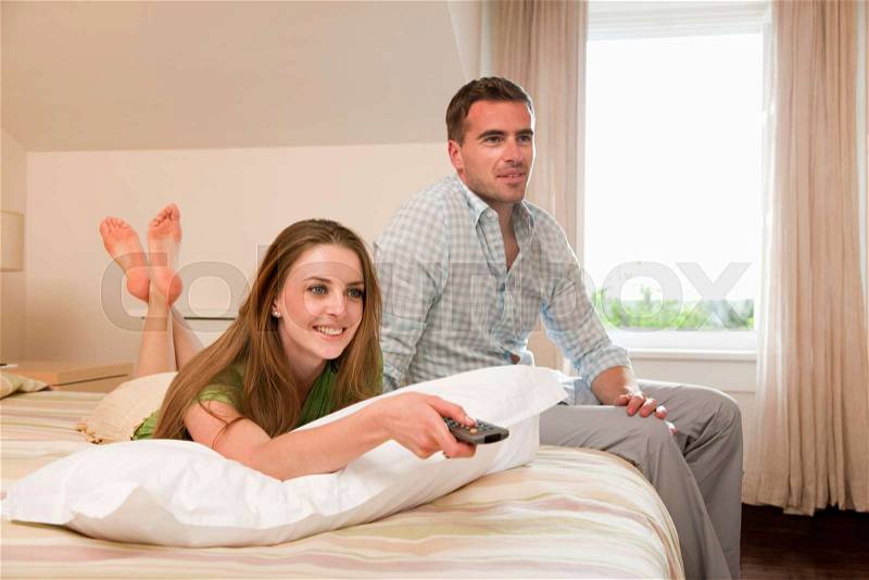 Couple in hotel room watching TV, stock photo