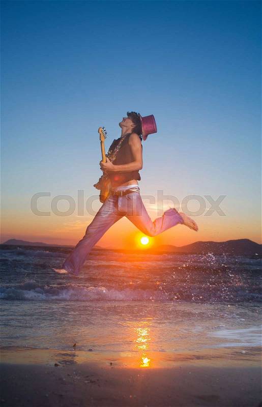 Young man jumps with guitar at sunset, stock photo