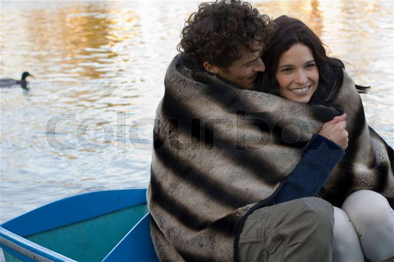 Man and woman snuggling under blanket, stock photo