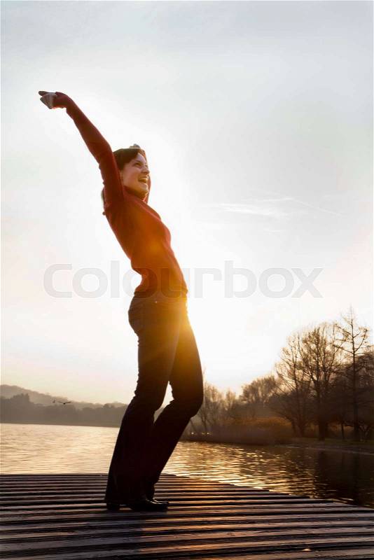 Woman cheering on jetty over lake, stock photo