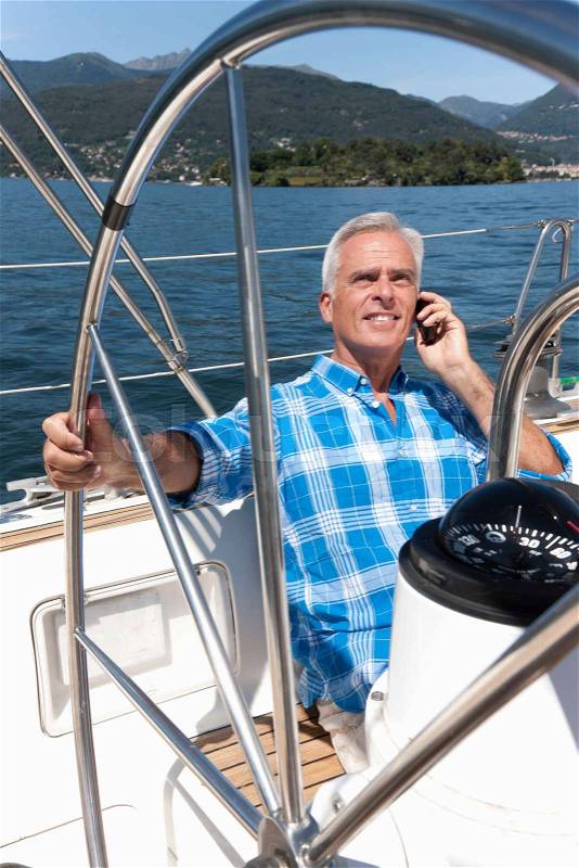 Older man talking on phone on sailboat, stock photo