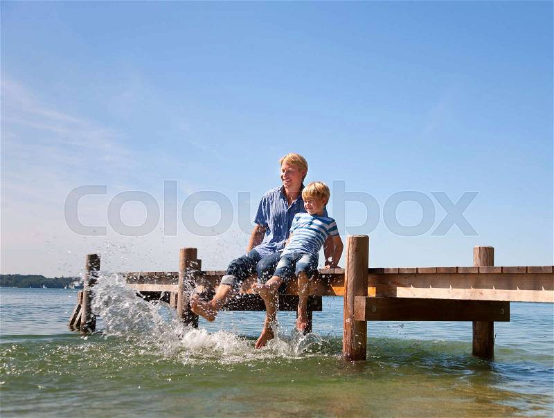 Father and son dangling feet in lake, stock photo