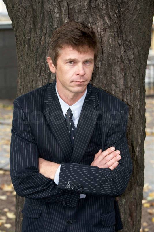 Man leaning against tree in city, arms crossed, stock photo
