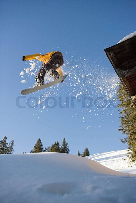 A snowboarder jumping off a cabin roof, stock photo