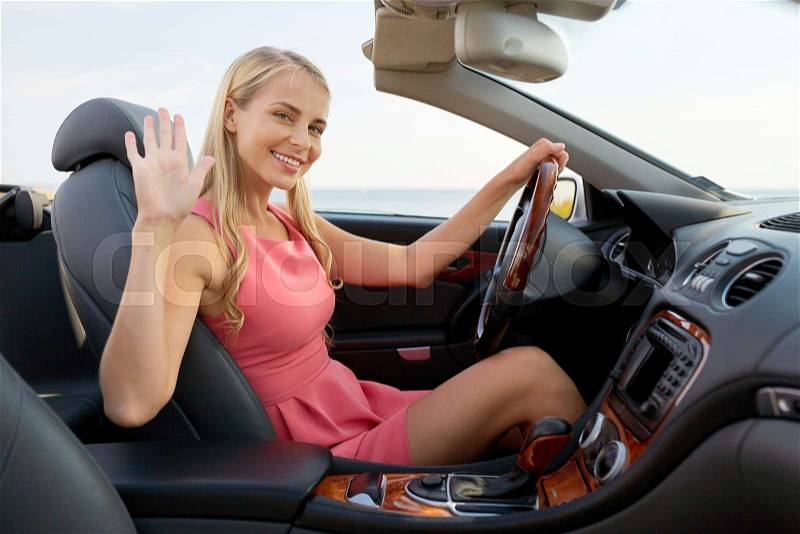 Travel, road trip and people concept - happy young woman in convertible car waving hand, stock photo