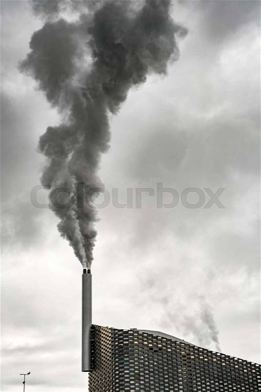 Copenhagen Copenhill waste-to-energy plant with steaming chimney on the background of the cloudy gray sky. Vertical, stock photo